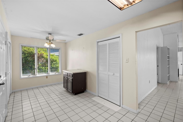 interior space featuring light tile patterned floors, visible vents, a ceiling fan, and baseboards