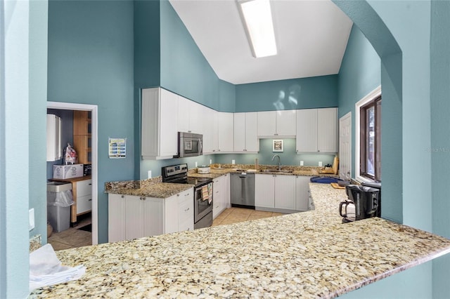 kitchen featuring a sink, appliances with stainless steel finishes, white cabinets, light stone countertops, and a towering ceiling