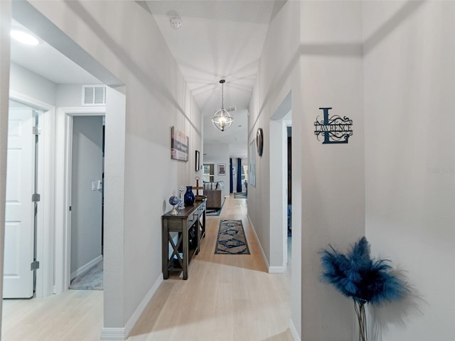 hallway featuring visible vents, an inviting chandelier, baseboards, and wood finished floors