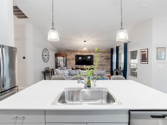 kitchen with a sink, open floor plan, appliances with stainless steel finishes, light countertops, and an accent wall