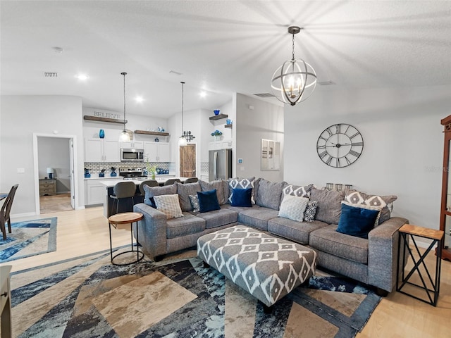 living area featuring visible vents, light wood-style flooring, an inviting chandelier, and vaulted ceiling