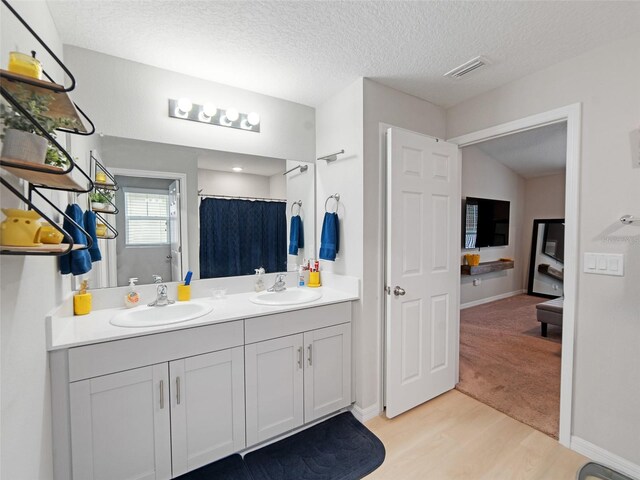 full bathroom with double vanity, visible vents, wood finished floors, and a sink