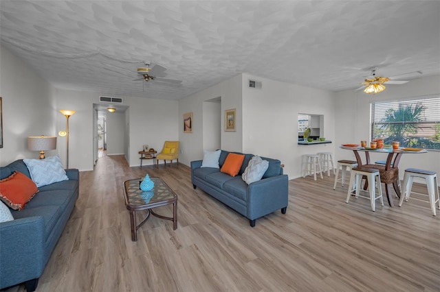 living room featuring visible vents, wood finished floors, a textured ceiling, and ceiling fan