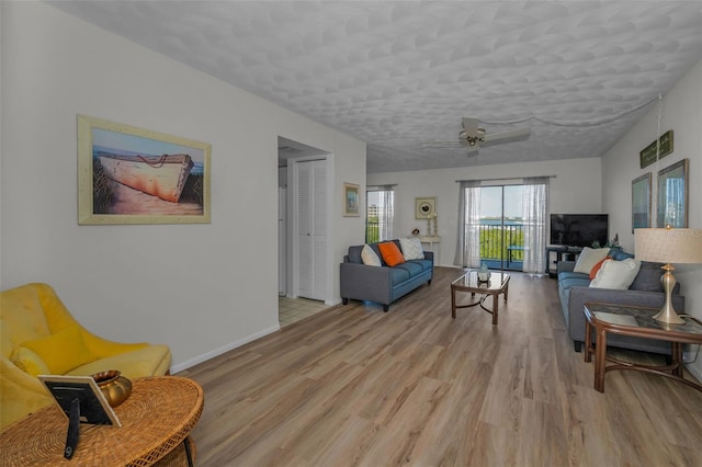 living room featuring baseboards, a textured ceiling, light wood-style flooring, and a ceiling fan