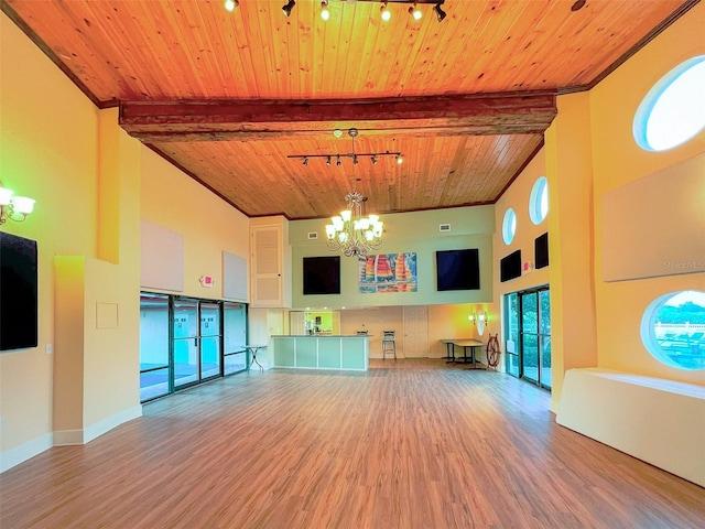 unfurnished living room featuring a notable chandelier, wood finished floors, rail lighting, wood ceiling, and a towering ceiling