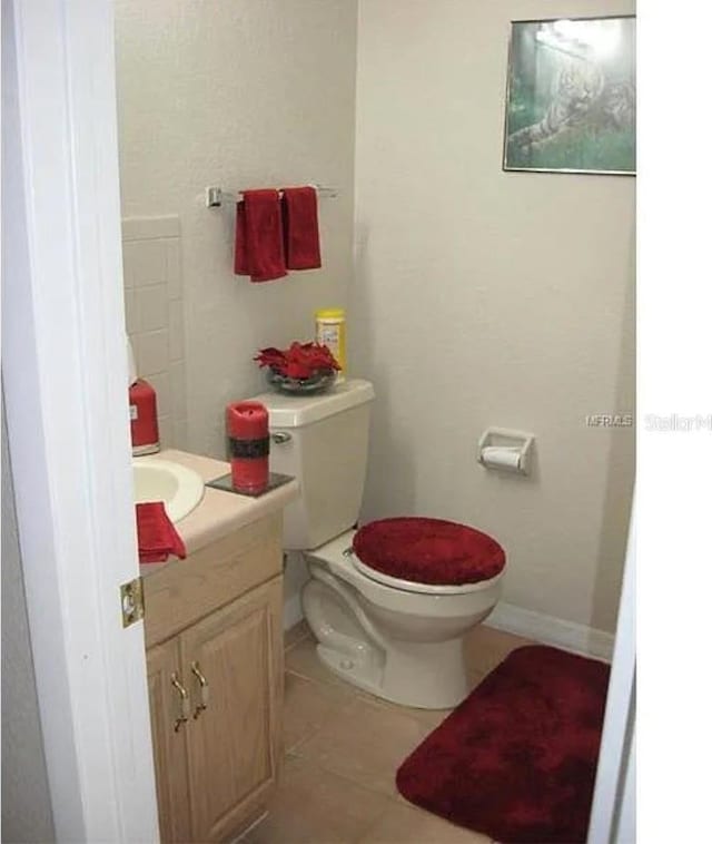 half bath featuring tile patterned floors, baseboards, toilet, and vanity