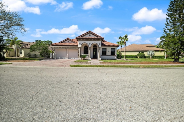 mediterranean / spanish home with stucco siding, an attached garage, a tile roof, and decorative driveway