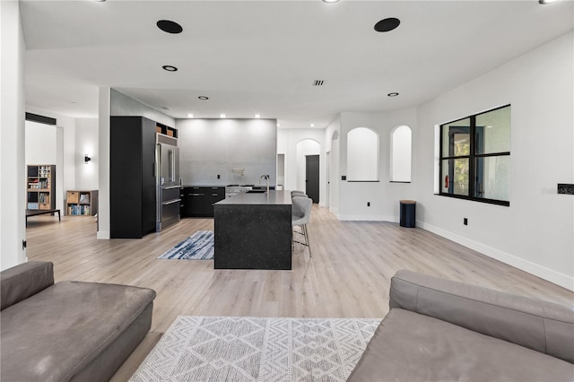 living room with recessed lighting, light wood-type flooring, arched walkways, and baseboards