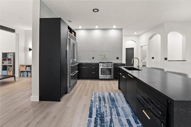 kitchen with light wood-type flooring, high quality appliances, a sink, recessed lighting, and dark cabinets