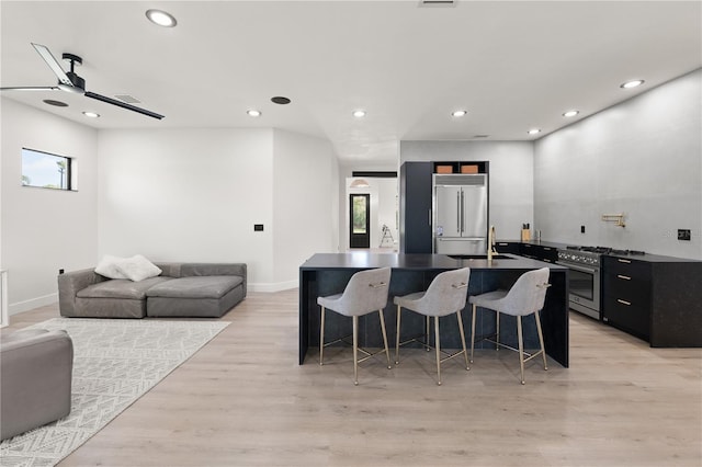 kitchen with a breakfast bar, premium appliances, a sink, dark countertops, and open floor plan