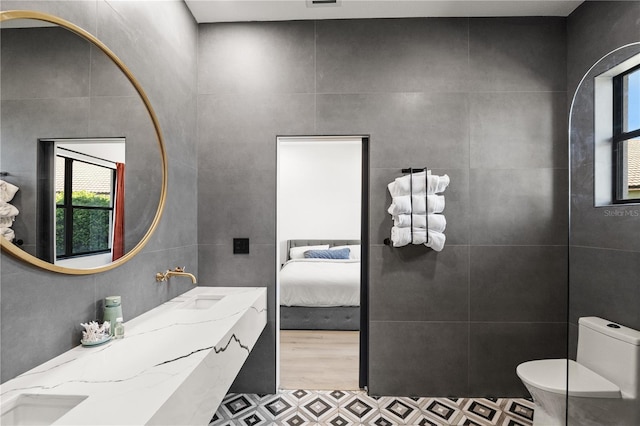 bathroom featuring toilet, ensuite bathroom, a sink, wood finished floors, and tile walls