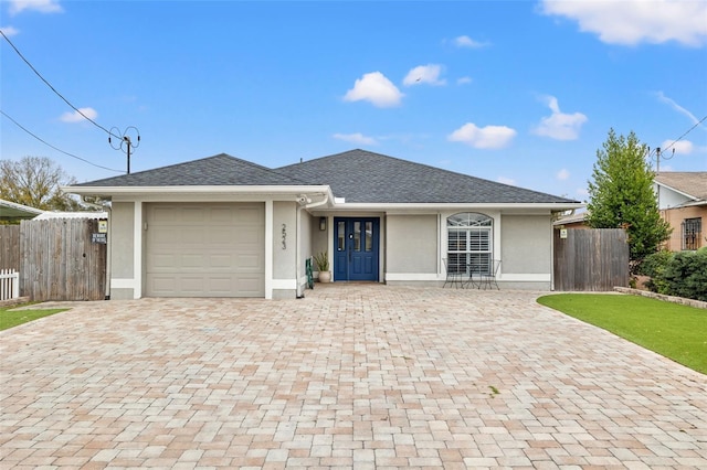 ranch-style home featuring fence, roof with shingles, stucco siding, decorative driveway, and an attached garage