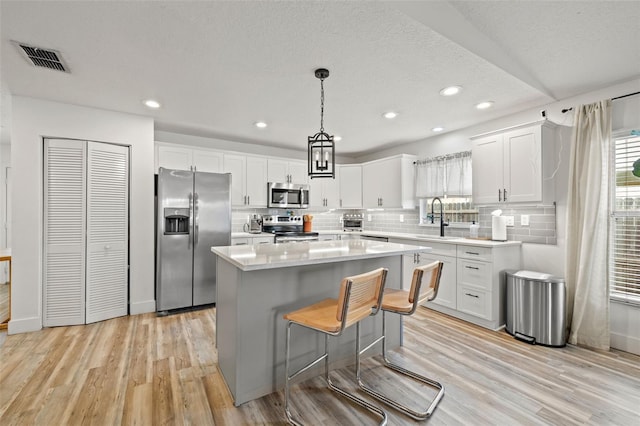 kitchen featuring visible vents, a center island, white cabinetry, appliances with stainless steel finishes, and light wood finished floors