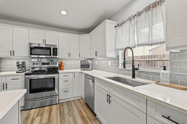 kitchen featuring light wood finished floors, a sink, stainless steel appliances, white cabinetry, and tasteful backsplash