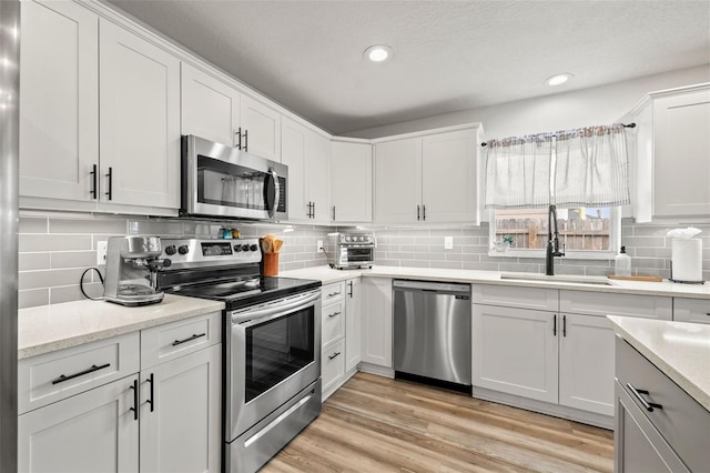 kitchen featuring a sink, backsplash, white cabinetry, light wood-style floors, and appliances with stainless steel finishes