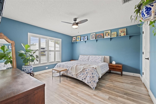 bedroom with a ceiling fan, light wood-style floors, baseboards, and a textured ceiling