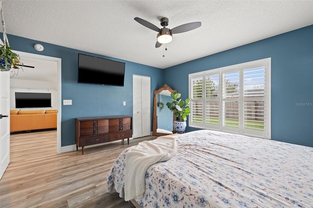 bedroom with wood finished floors, baseboards, ceiling fan, a closet, and a textured ceiling