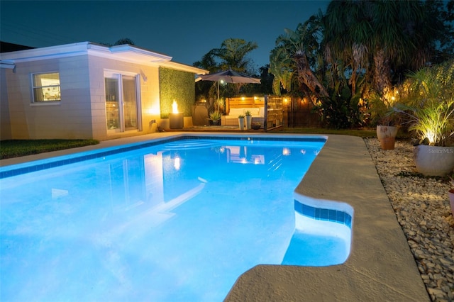 pool at night featuring fence and an outdoor pool