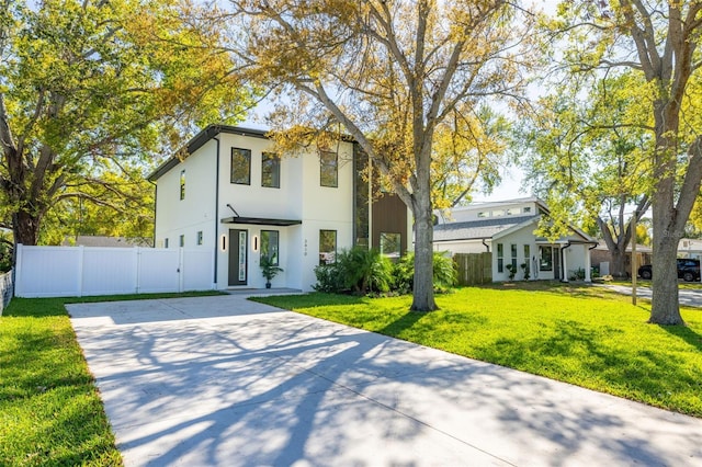 view of front of house featuring stucco siding, concrete driveway, a front yard, and fence