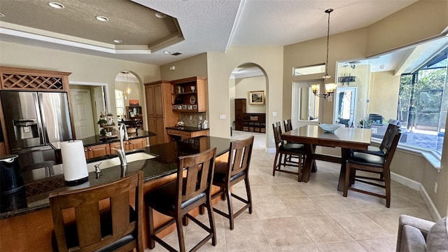 dining space featuring a tray ceiling, arched walkways, an inviting chandelier, light tile patterned floors, and baseboards