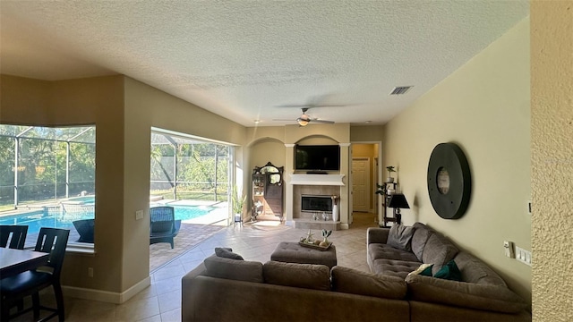 living area with visible vents, a tiled fireplace, light tile patterned floors, a textured ceiling, and a ceiling fan