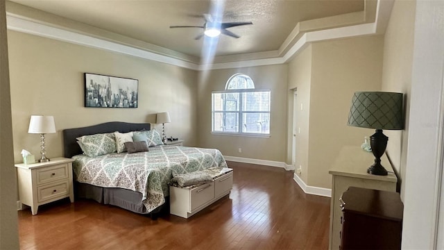 bedroom with a tray ceiling, ceiling fan, dark wood-type flooring, and baseboards