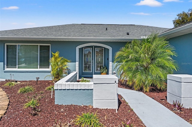 entrance to property featuring french doors, roof with shingles, and stucco siding