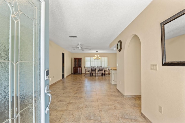 corridor featuring visible vents, a notable chandelier, a textured ceiling, arched walkways, and light tile patterned floors