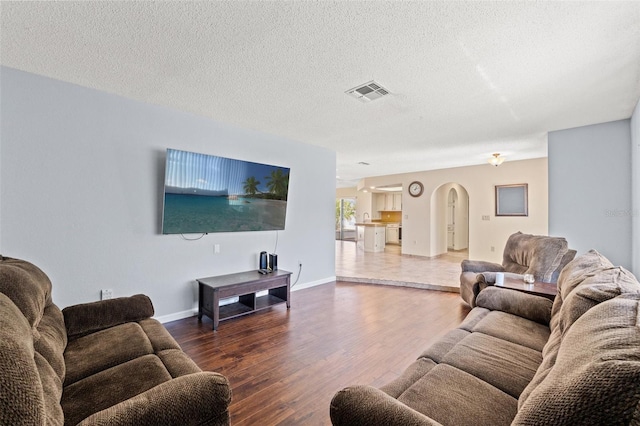 living area featuring wood finished floors, baseboards, visible vents, arched walkways, and a textured ceiling