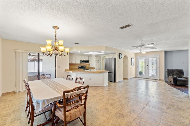 dining space featuring visible vents, ceiling fan with notable chandelier, french doors, arched walkways, and a textured ceiling