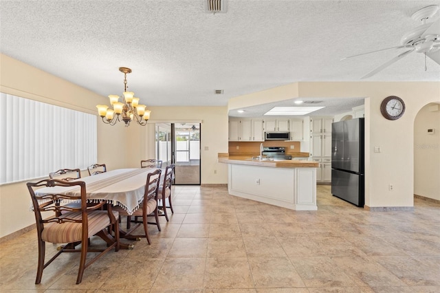 dining room featuring visible vents, baseboards, ceiling fan with notable chandelier, arched walkways, and a textured ceiling