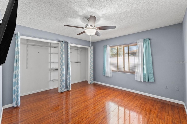 unfurnished bedroom with ceiling fan, baseboards, wood finished floors, and multiple closets