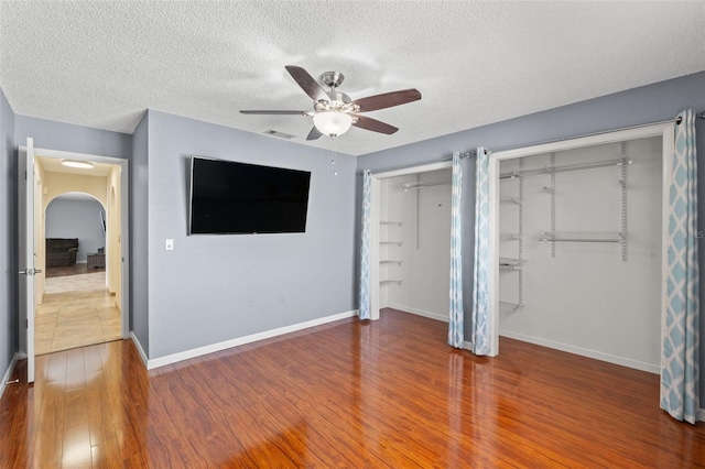 unfurnished bedroom with arched walkways, two closets, baseboards, and wood finished floors