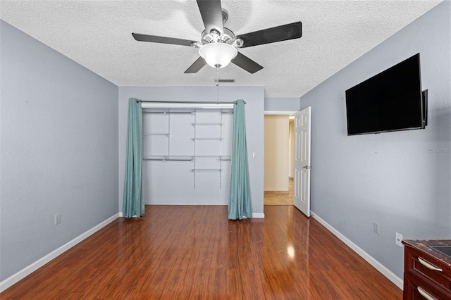 unfurnished bedroom with wood finished floors, baseboards, ceiling fan, a closet, and a textured ceiling