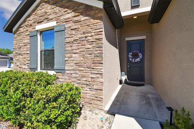 view of exterior entry with stone siding, stucco siding, and visible vents