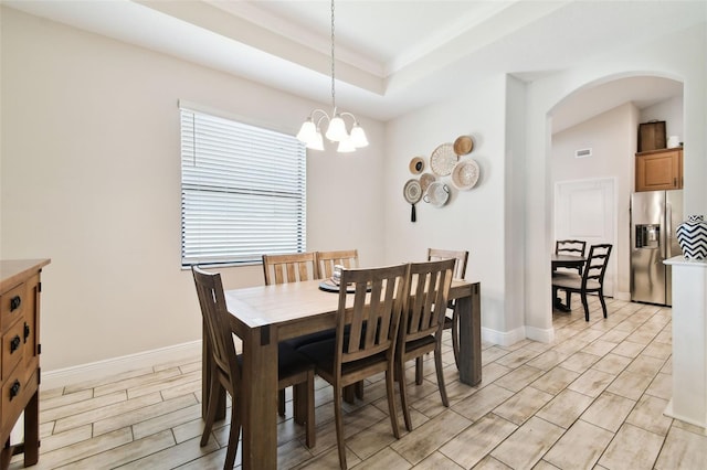 dining space featuring a tray ceiling, a notable chandelier, baseboards, and arched walkways