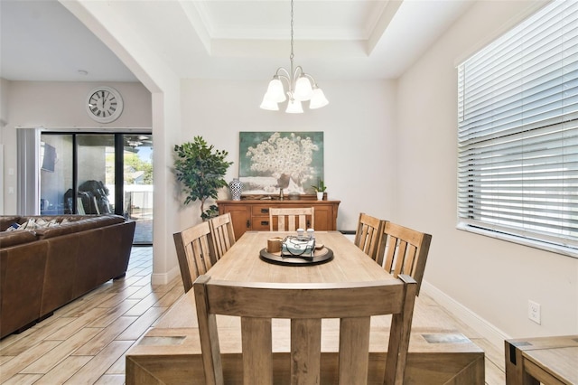 dining area featuring light wood-type flooring, a raised ceiling, arched walkways, an inviting chandelier, and baseboards