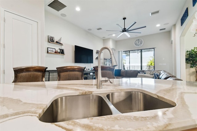 kitchen featuring light stone counters, open floor plan, visible vents, and a sink