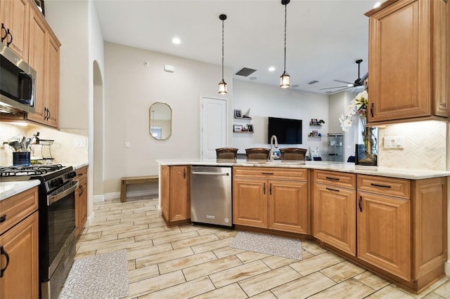 kitchen with ceiling fan, decorative backsplash, appliances with stainless steel finishes, a peninsula, and a sink