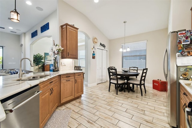 kitchen with light stone counters, arched walkways, a sink, appliances with stainless steel finishes, and a chandelier