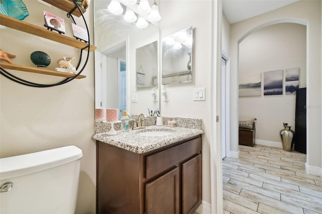 half bathroom featuring vanity, toilet, baseboards, and wood finish floors