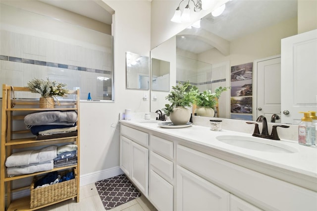 bathroom with double vanity, walk in shower, baseboards, and a sink