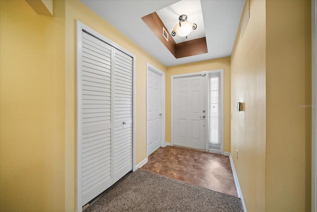 foyer entrance featuring visible vents, baseboards, a tray ceiling, carpet flooring, and a skylight