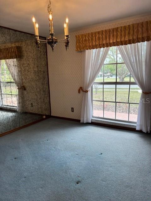 carpeted spare room with wallpapered walls, baseboards, and a chandelier