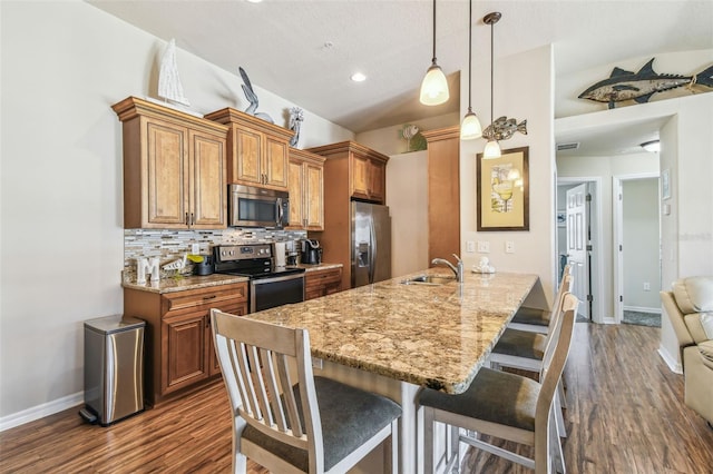 kitchen featuring a sink, brown cabinets, stainless steel appliances, a kitchen breakfast bar, and baseboards