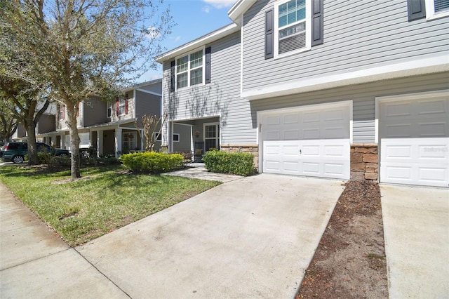 view of property featuring stone siding, an attached garage, driveway, and a front yard