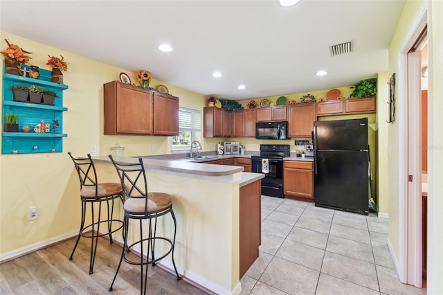 kitchen with visible vents, a breakfast bar, a peninsula, black appliances, and a sink