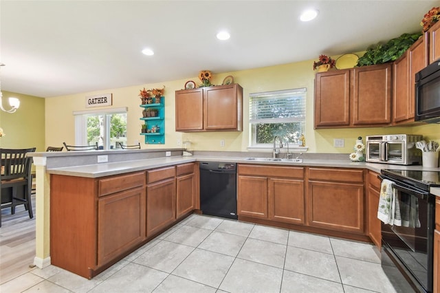 kitchen featuring a peninsula, a sink, black appliances, light countertops, and brown cabinets