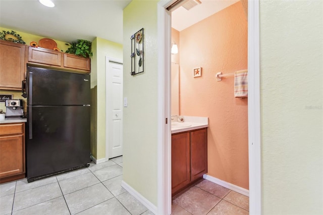 kitchen featuring light tile patterned floors, baseboards, visible vents, freestanding refrigerator, and a sink