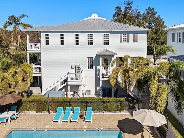 back of property with stairway, fence, a community pool, a patio area, and metal roof